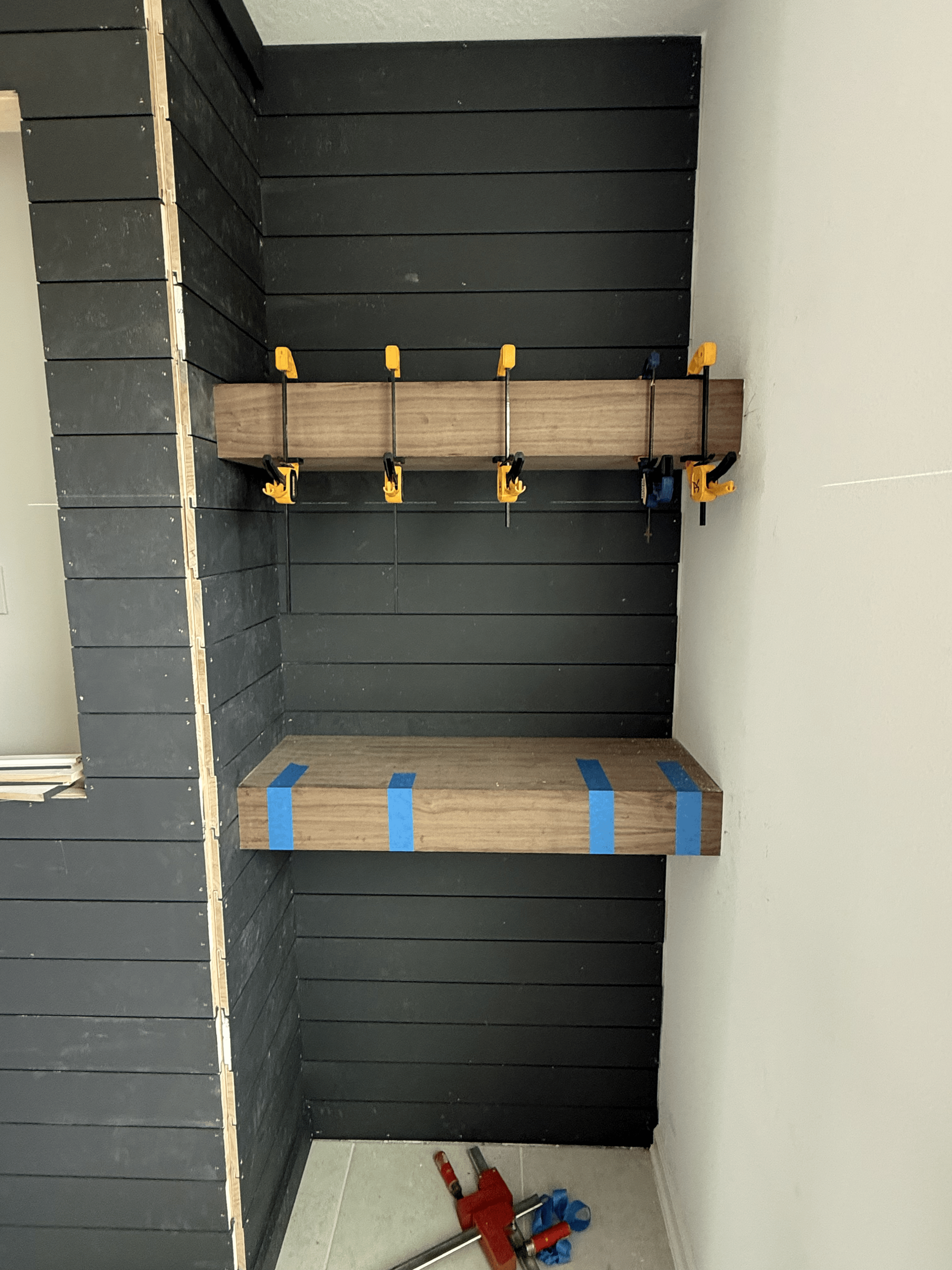 Wood shelves clamped in place against a black painted wall.