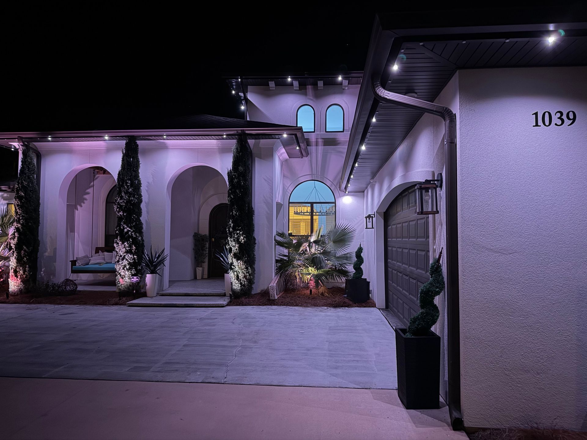 Night view of a stucco house with decorative lights, arched entryways, and a garage. Address number 1039 visible.
