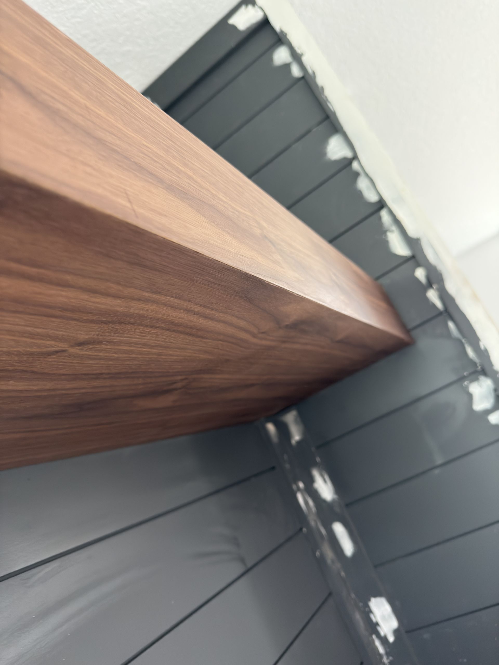 Wooden beam over dark gray panelled wall, with white paint flecks.