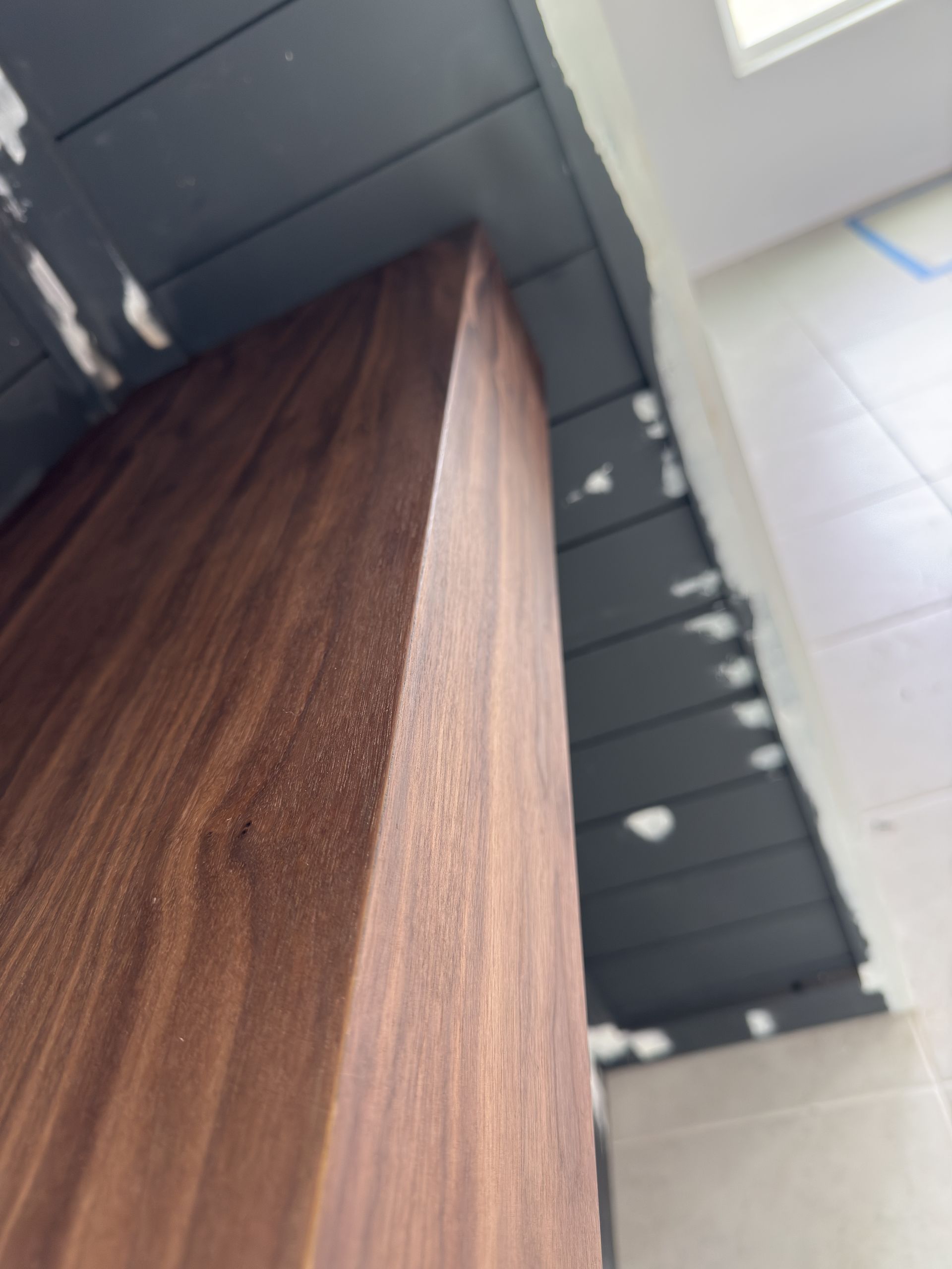 Dark wood cabinet corner against a dark gray horizontal paneled wall and a white wall, under construction.