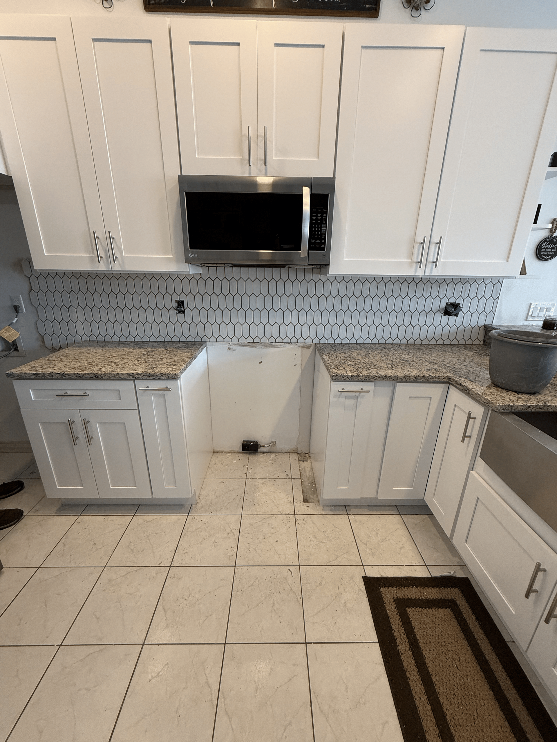 White kitchen cabinets, microwave, backsplash, and countertops with tiled floors and rug.