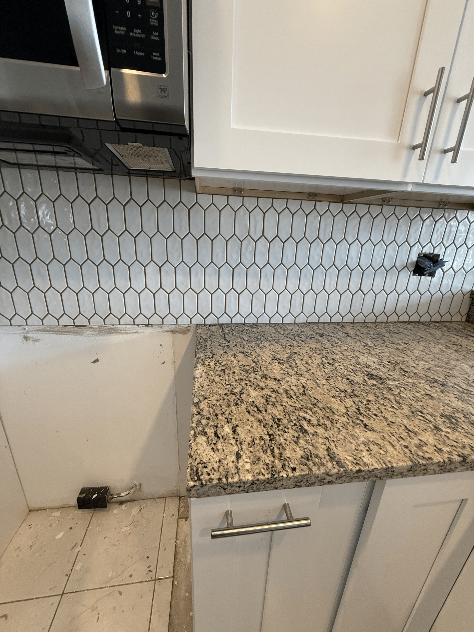 Kitchen with granite countertop, white cabinets, and white and black patterned backsplash.
