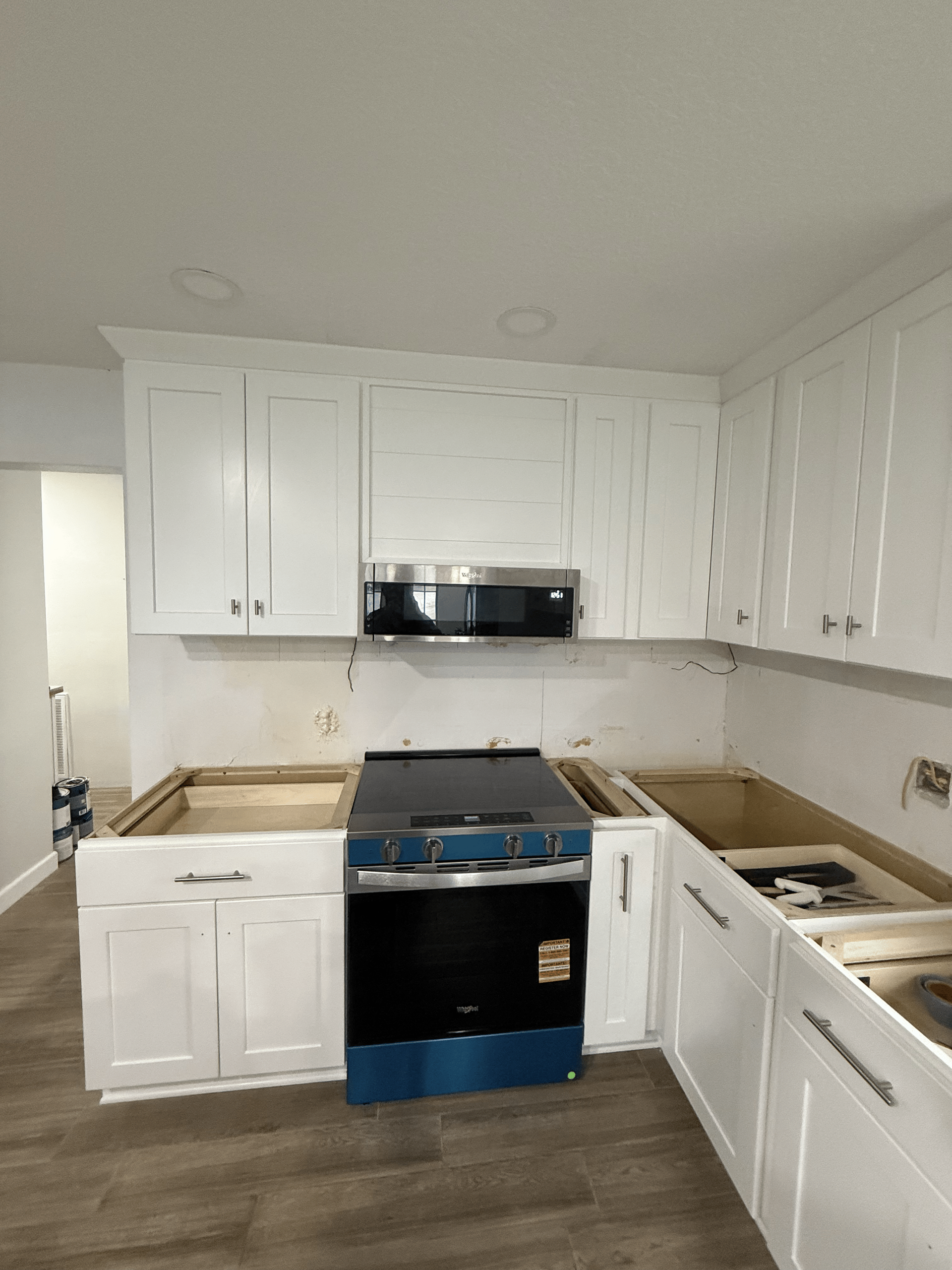 Kitchen renovation in progress: white cabinets, black oven, microwave, and missing countertops.