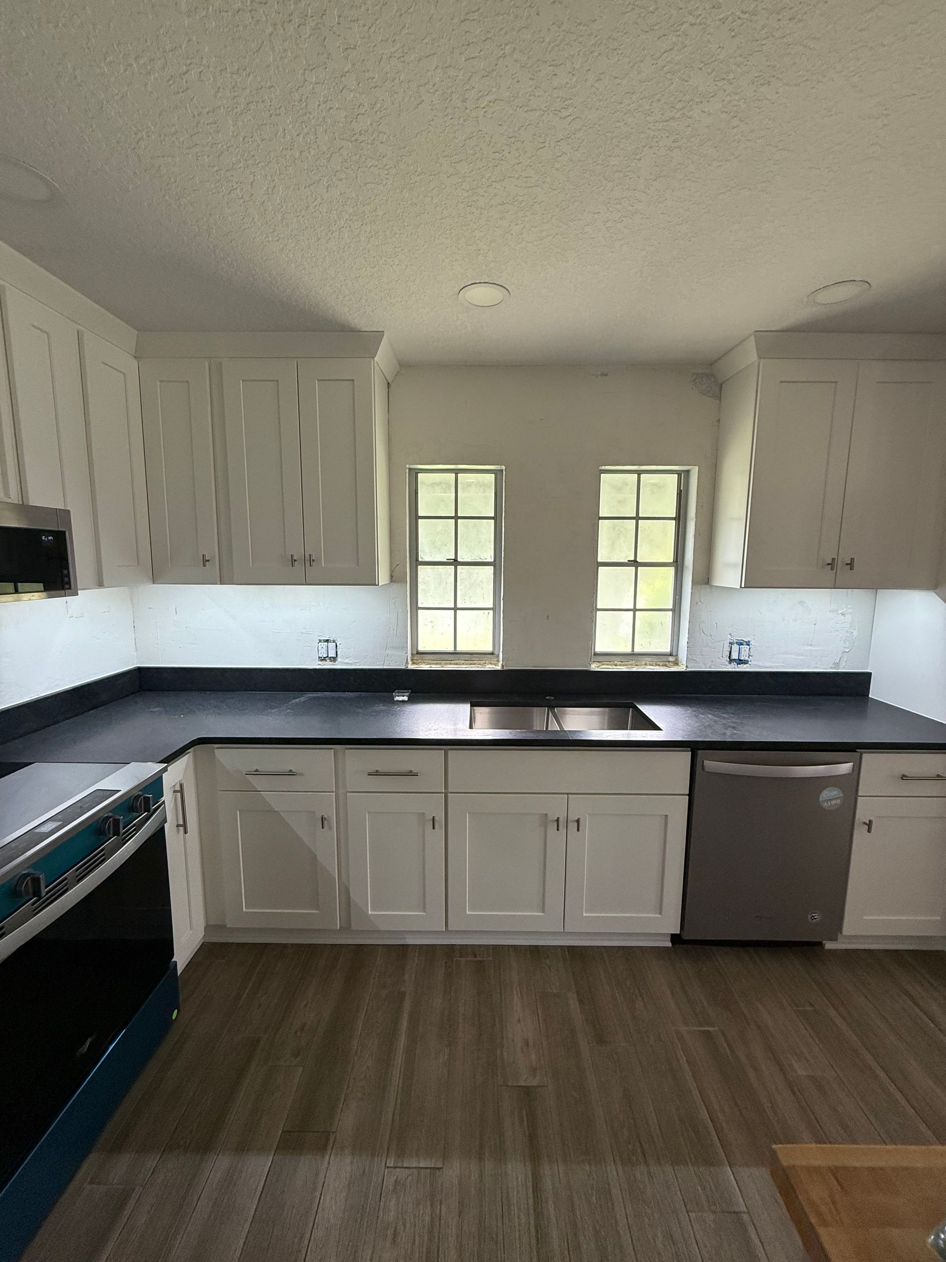 White kitchen with black countertops, stainless steel appliances, and two windows above the sink.