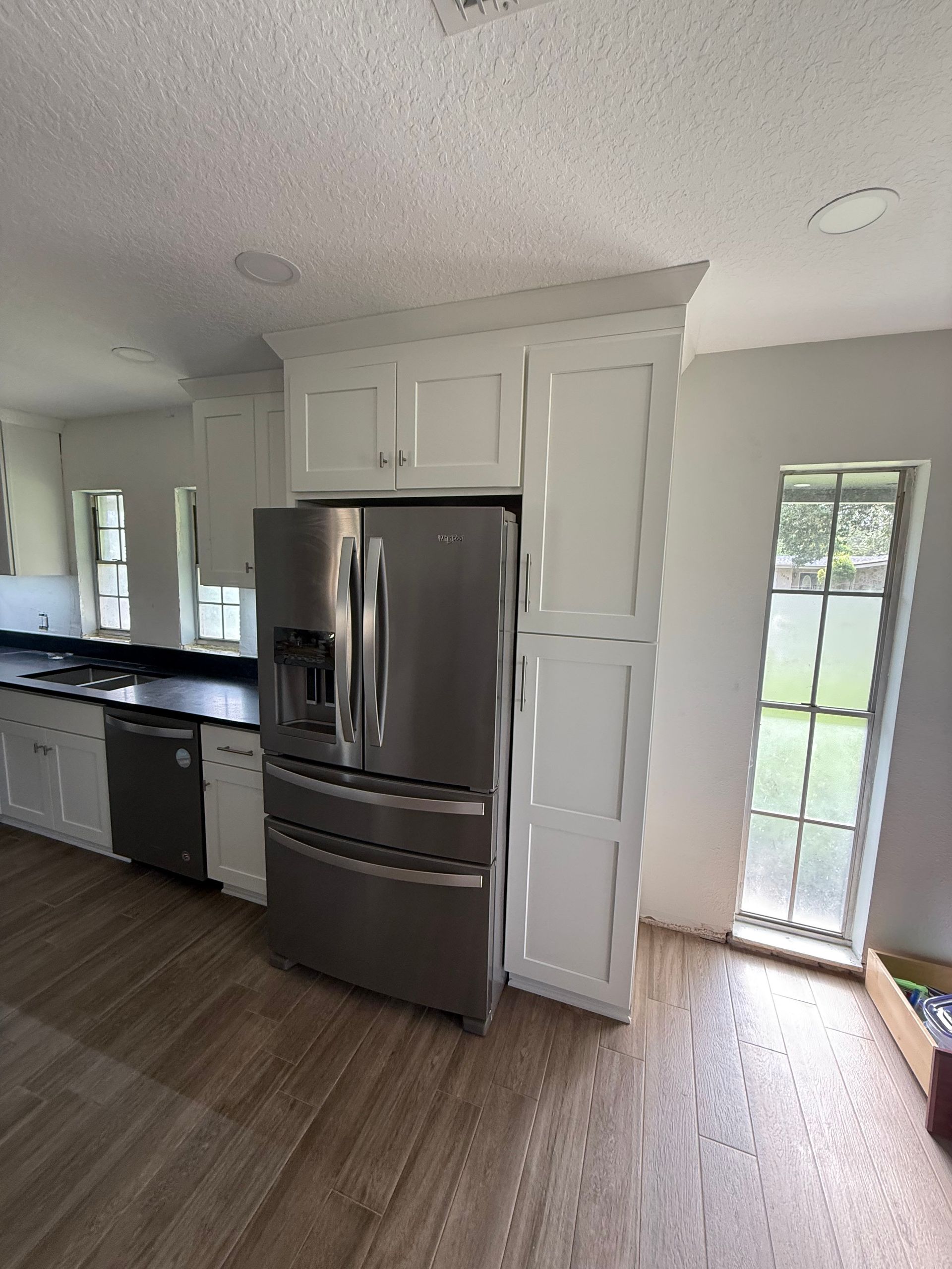 Stainless steel refrigerator in white kitchen with cabinets and window.