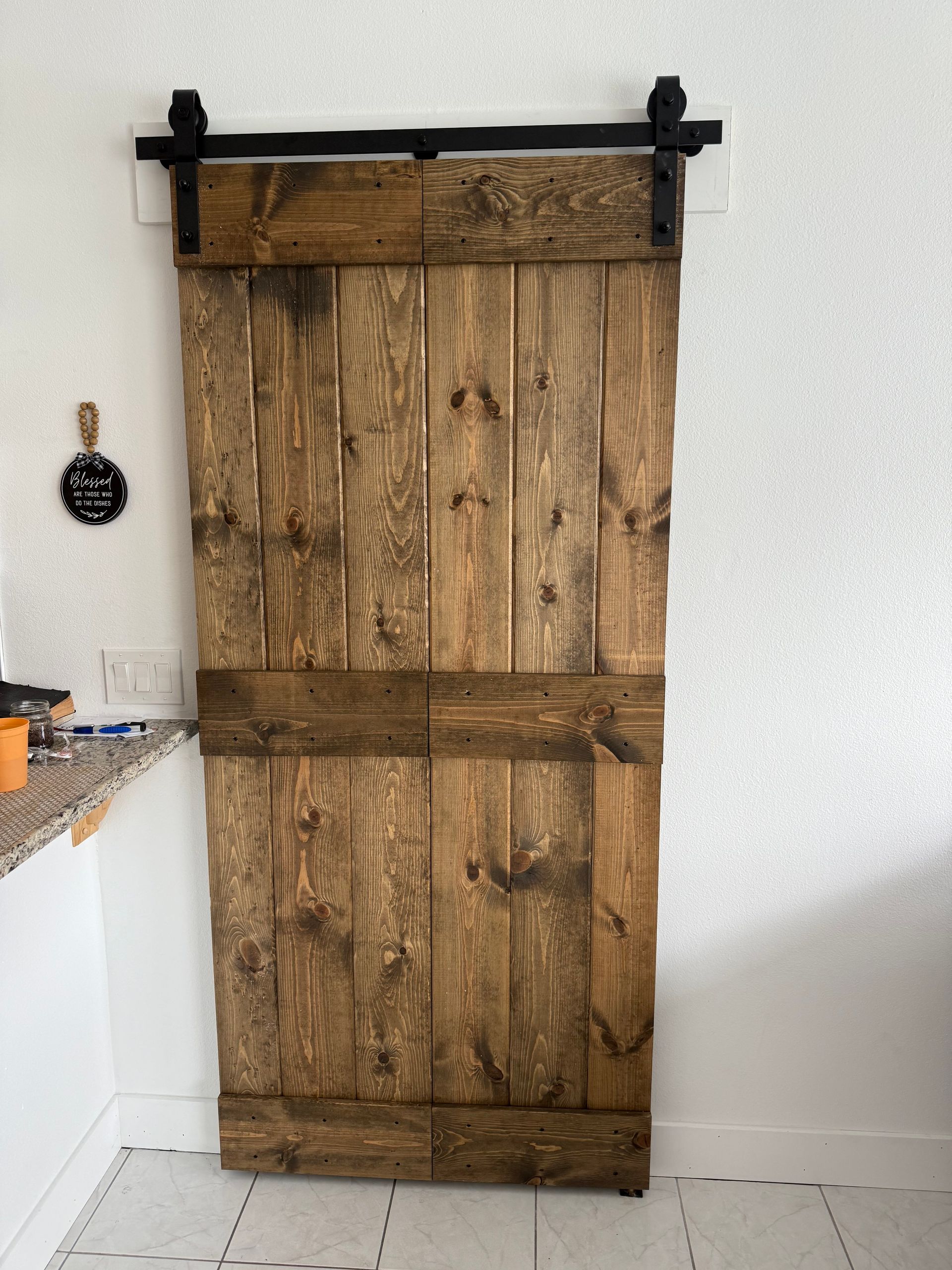 Barn door made of stained wood, mounted on a black sliding track, against a white wall.
