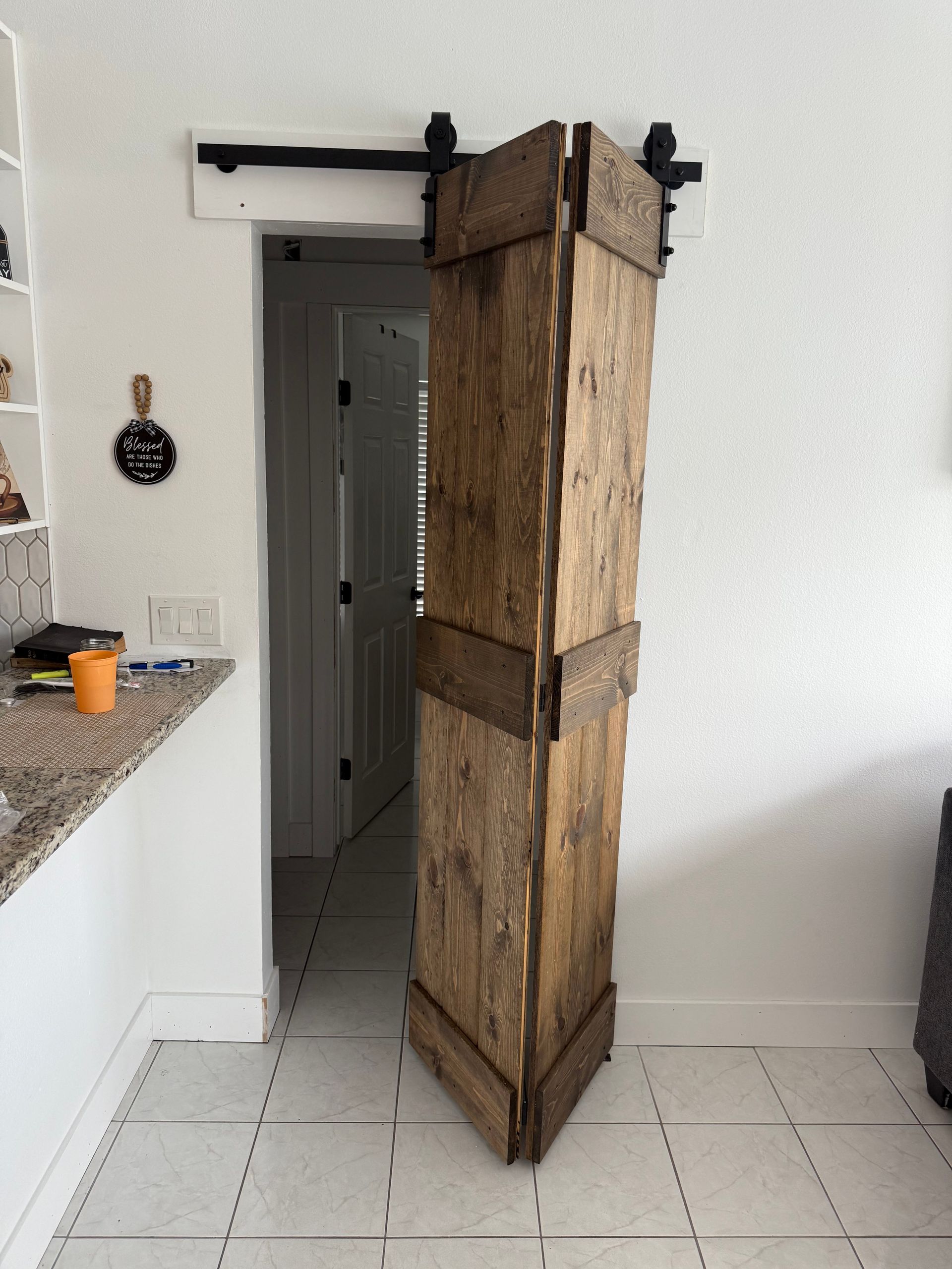 Barn door made of wood, mounted on a black sliding track, partially open in a white-walled room.