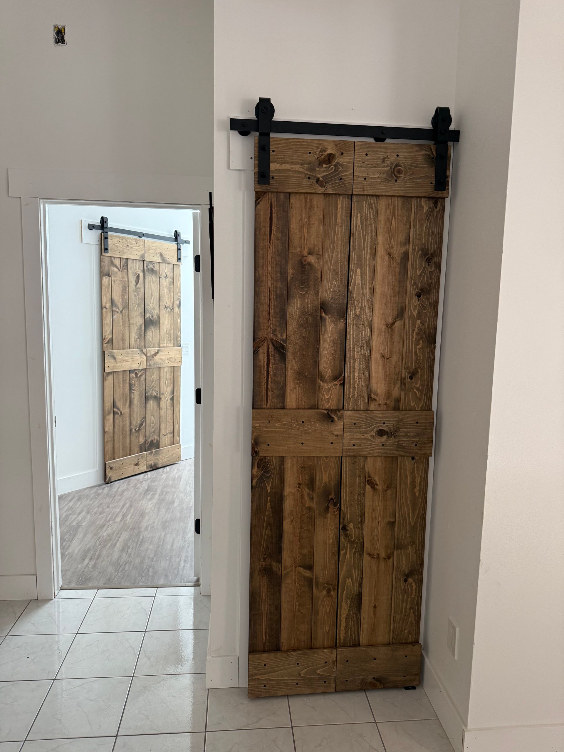 Barn doors on track, natural wood, open doorway, white walls and floor tiles.