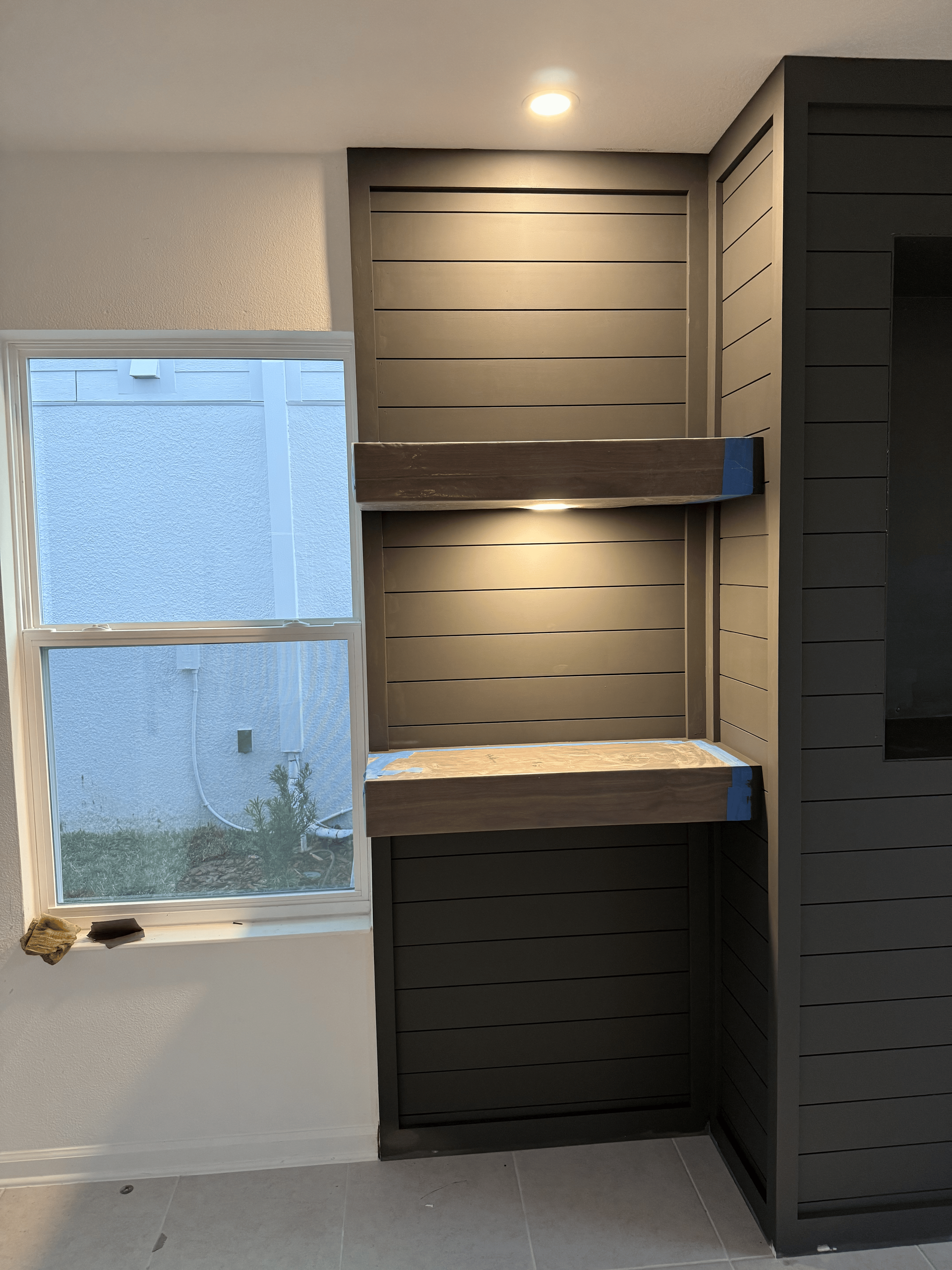 Built-in shelves with integrated lighting, dark gray with horizontal design, next to a window.