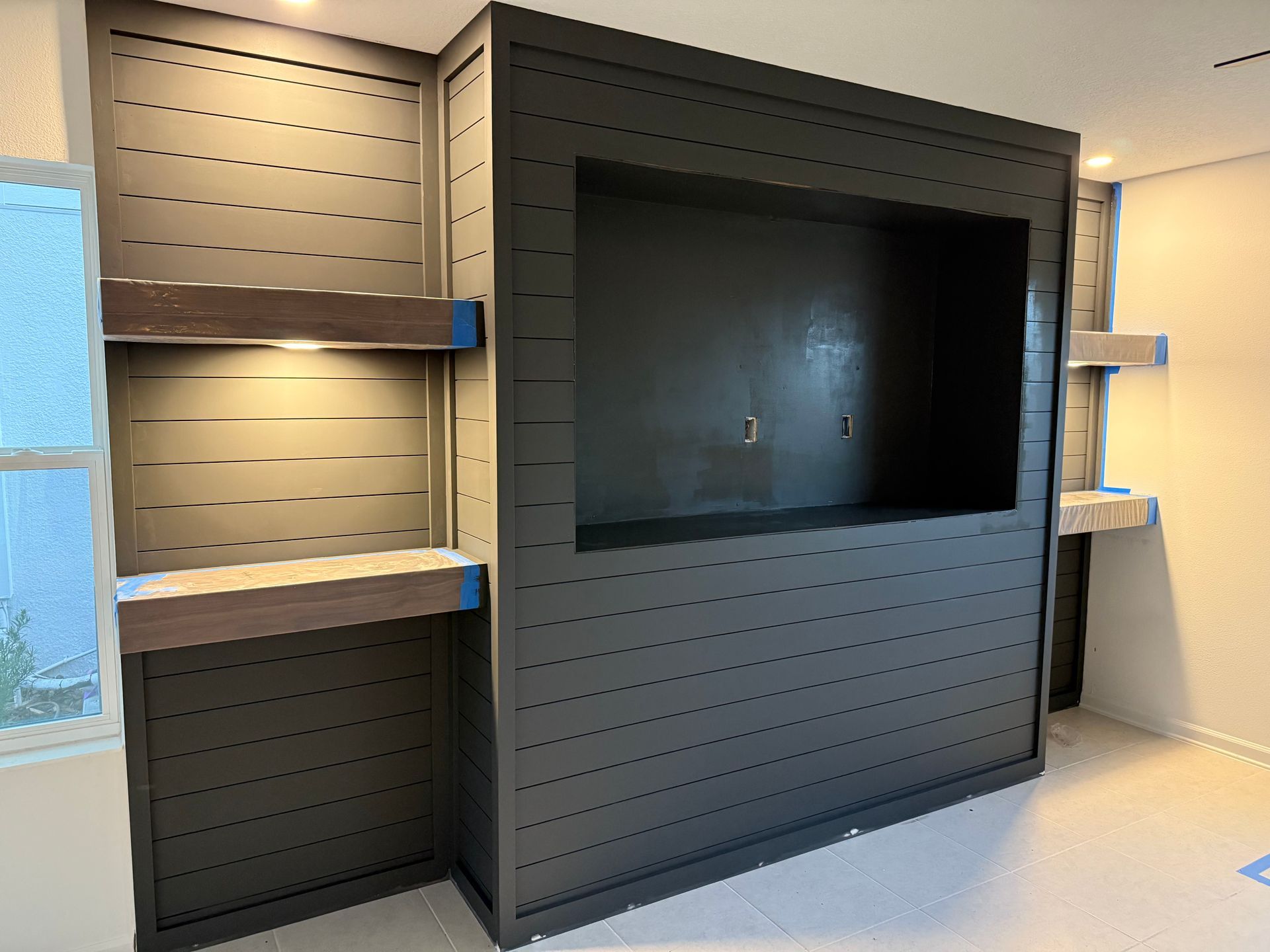 Built-in black media center with shelves, a rectangular opening, and wood accents. Construction in progress, indoor setting.