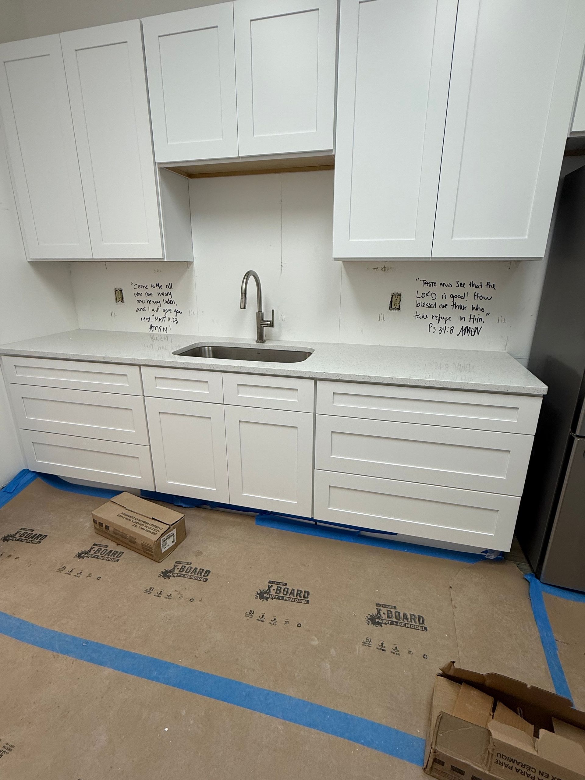 White kitchen cabinets and countertop, sink, and faucet. Construction zone with paper flooring.
