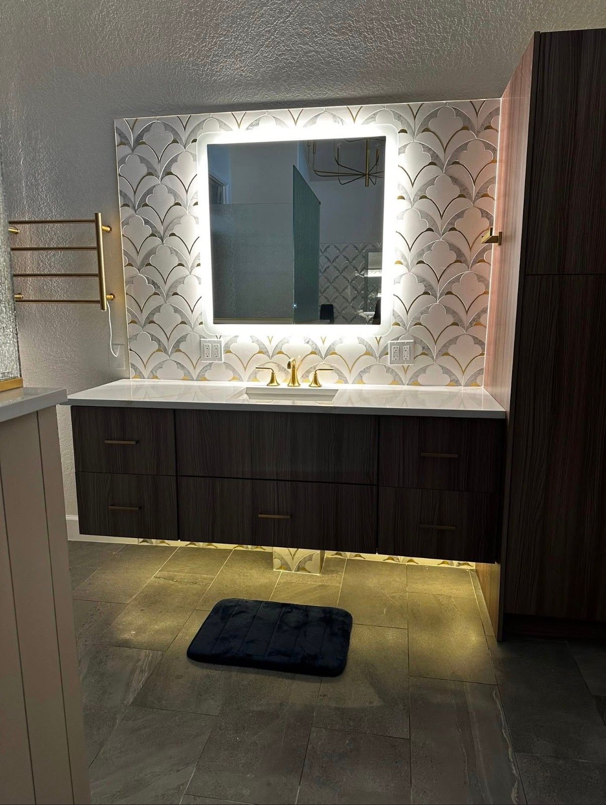 Modern bathroom with floating dark wood vanity, illuminated mirror, and patterned backsplash.