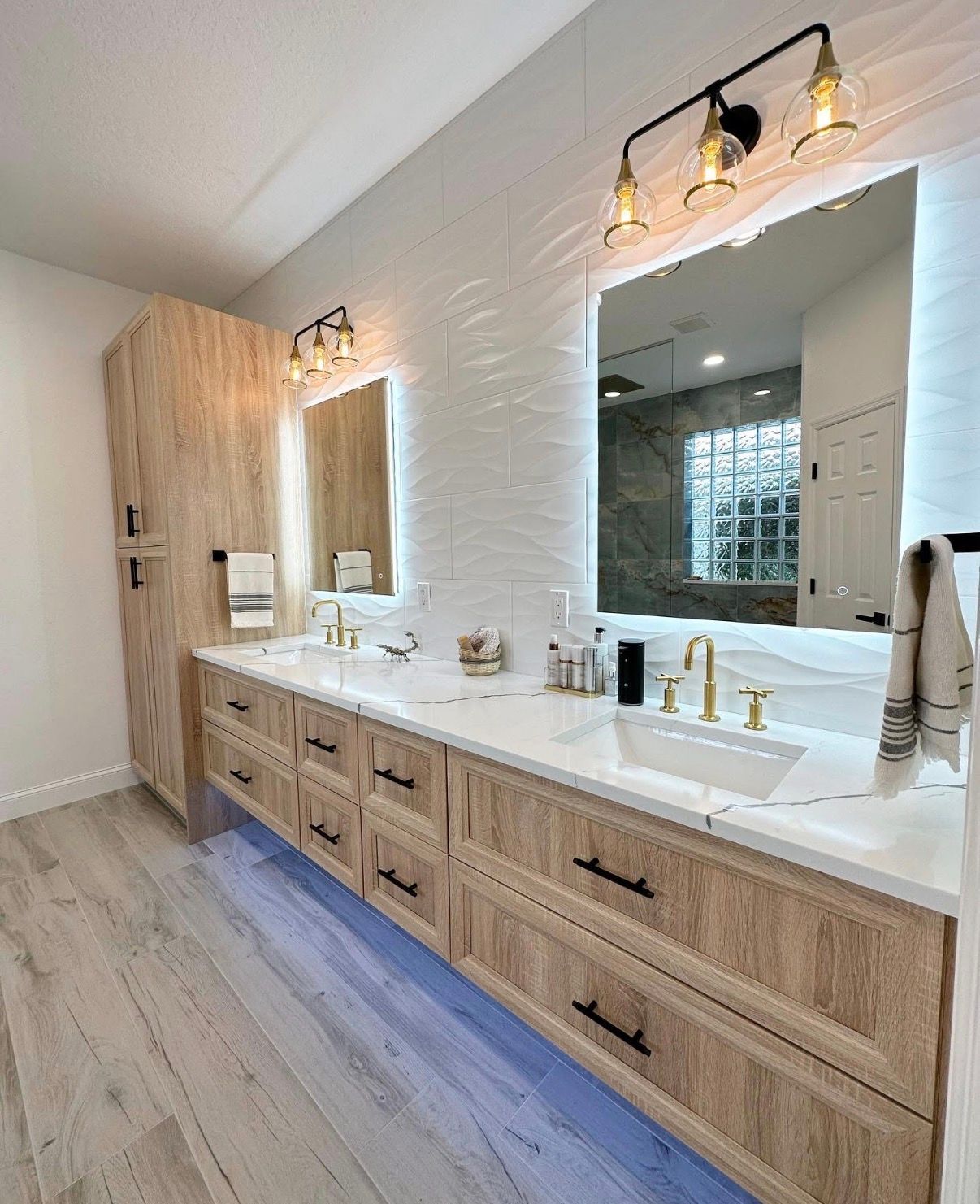 Modern bathroom with light wood cabinetry, white countertops, and backlit mirrors.