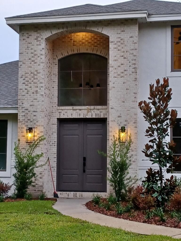 Brick-faced home entrance with dark double doors, arched window, and outdoor lights.