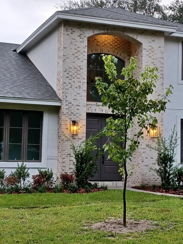 Two-story house with light brick and gray roof. Arched entrance with a tree in front.