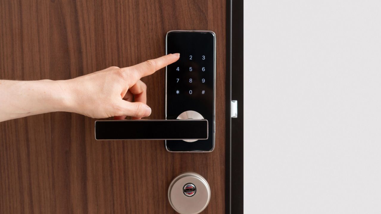 Hand entering code on a black digital door lock on a brown wooden door.