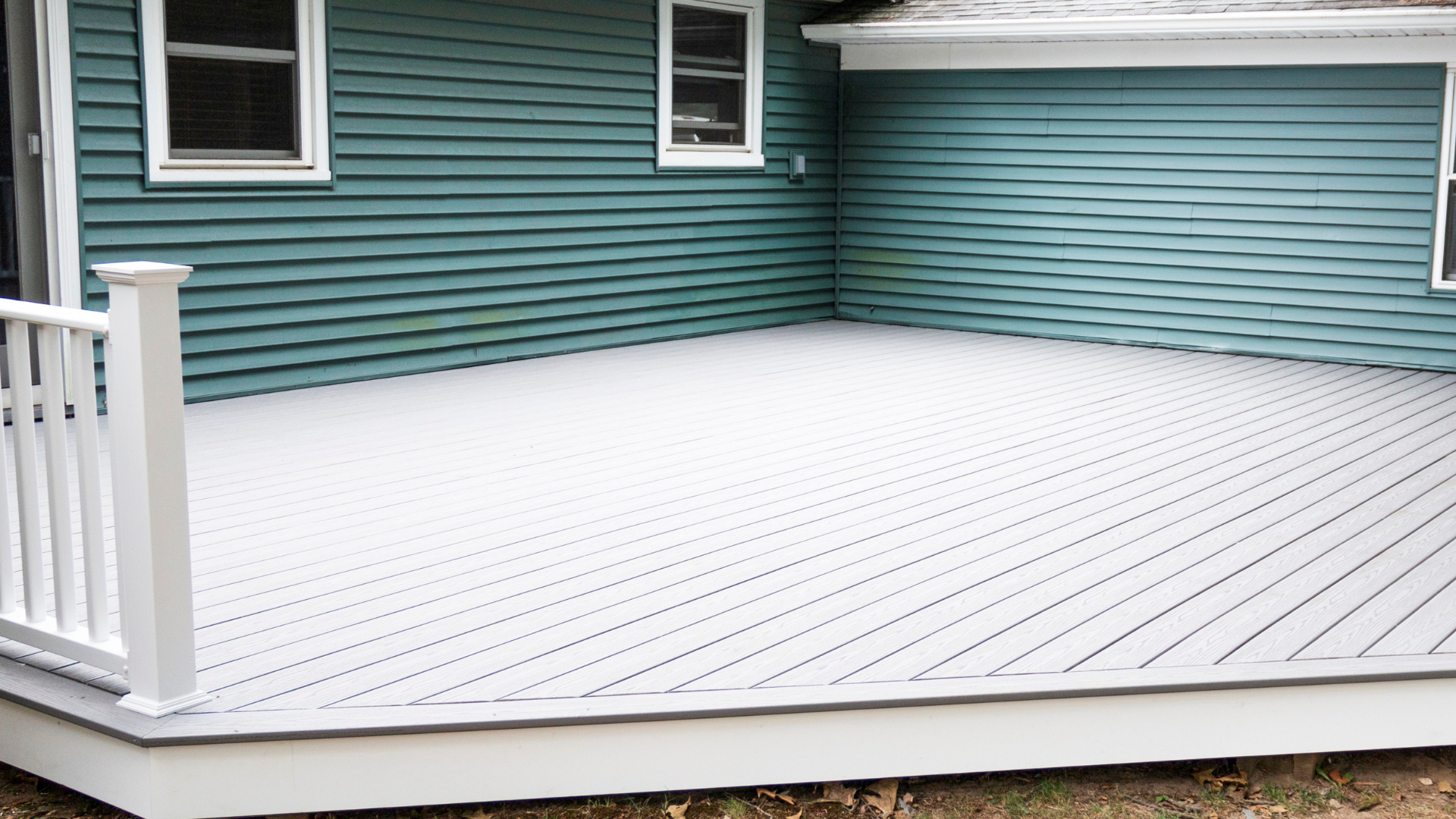 A gray composite deck extends from a teal siding house with white trim.