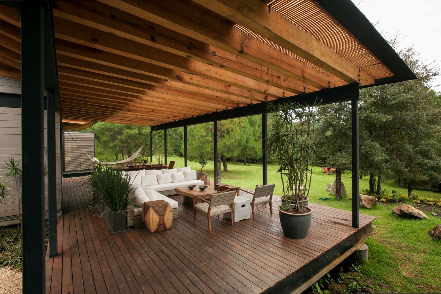 Covered wooden deck with outdoor seating overlooking a green lawn and trees.