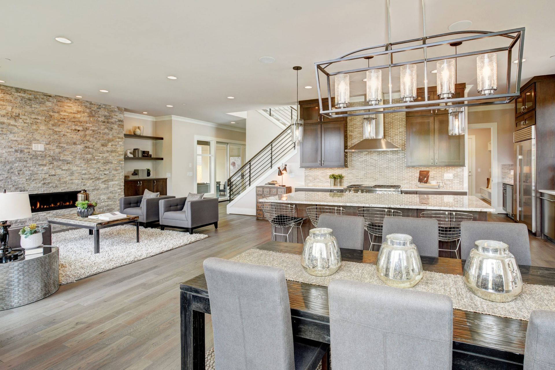 Open-concept kitchen and living area with gray cabinets, stone accent wall, and a long dining table.