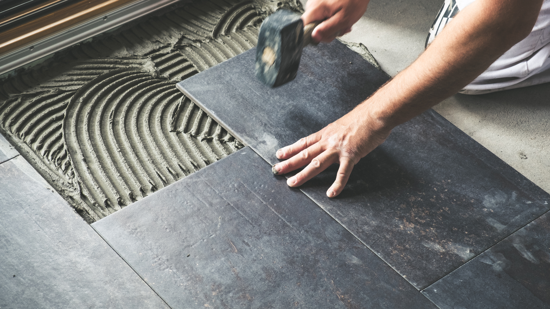 Person laying floor tiles, using a hammer to set the tile in place.