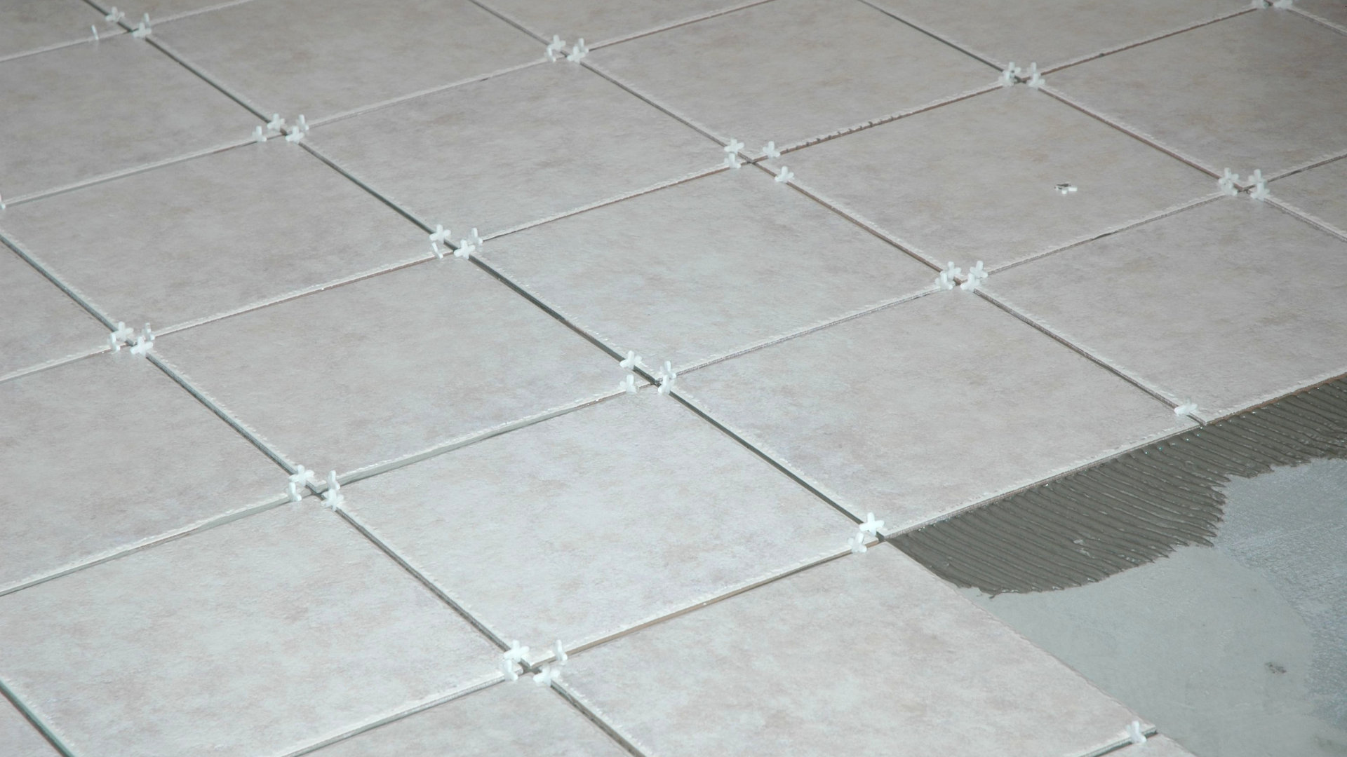Light-colored square tiles on a floor, separated by spacers, partially installed.
