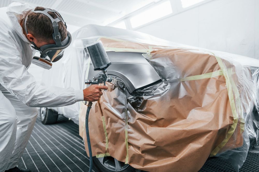 A Man Is Spray Painting A Car In A Garage — PK Crash Repairs In Uluru, NT