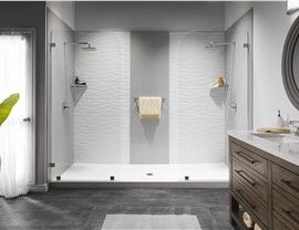 Modern bathroom with a large, white walk-in shower. Gray accent wall, glass doors, and dark gray tile flooring.