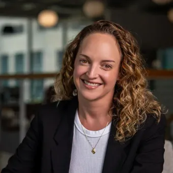 A woman with curly hair is wearing a black jacket and smiling for the camera.