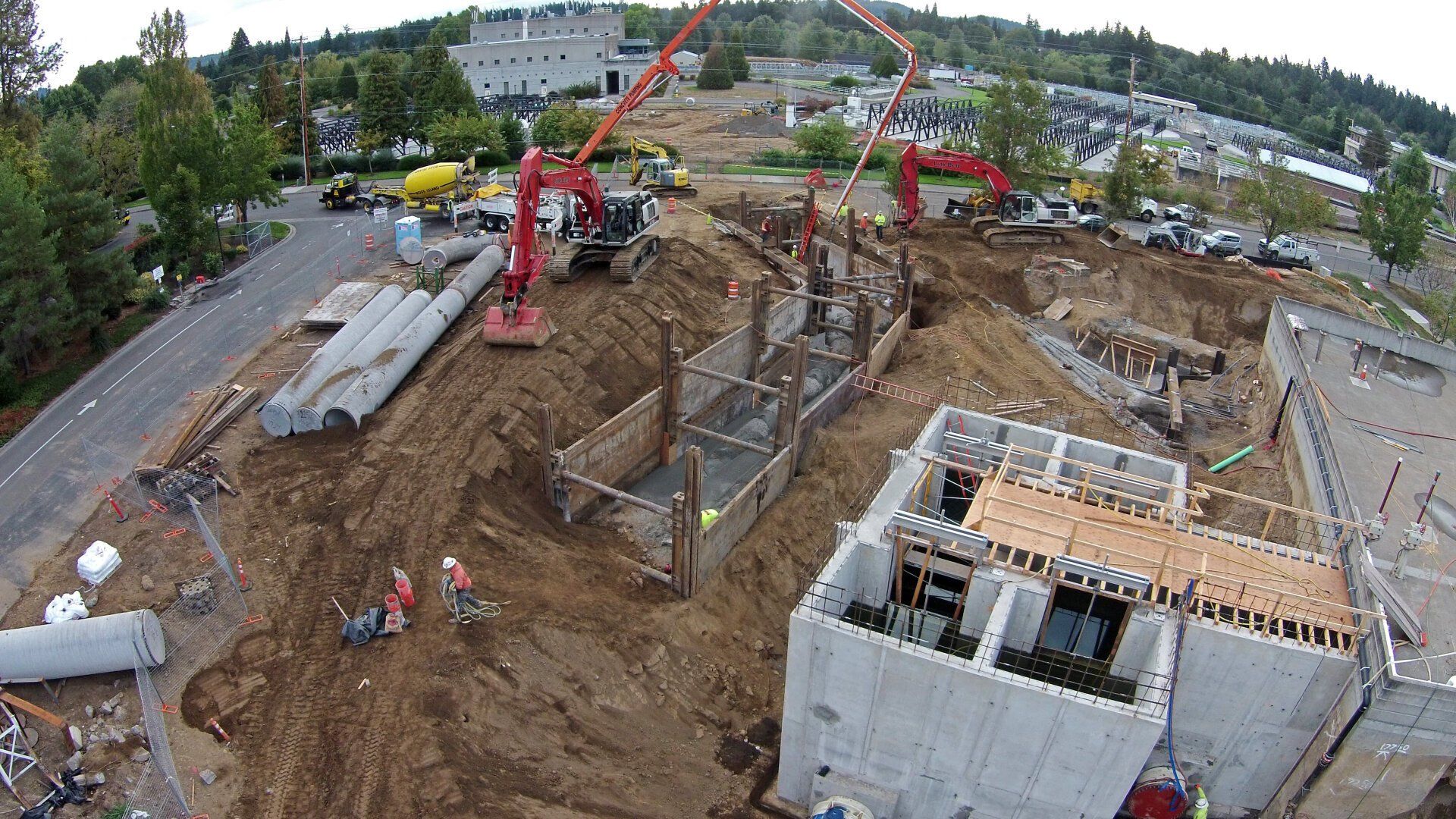 Construction site with workers, equipment, and concrete being poured into forms.