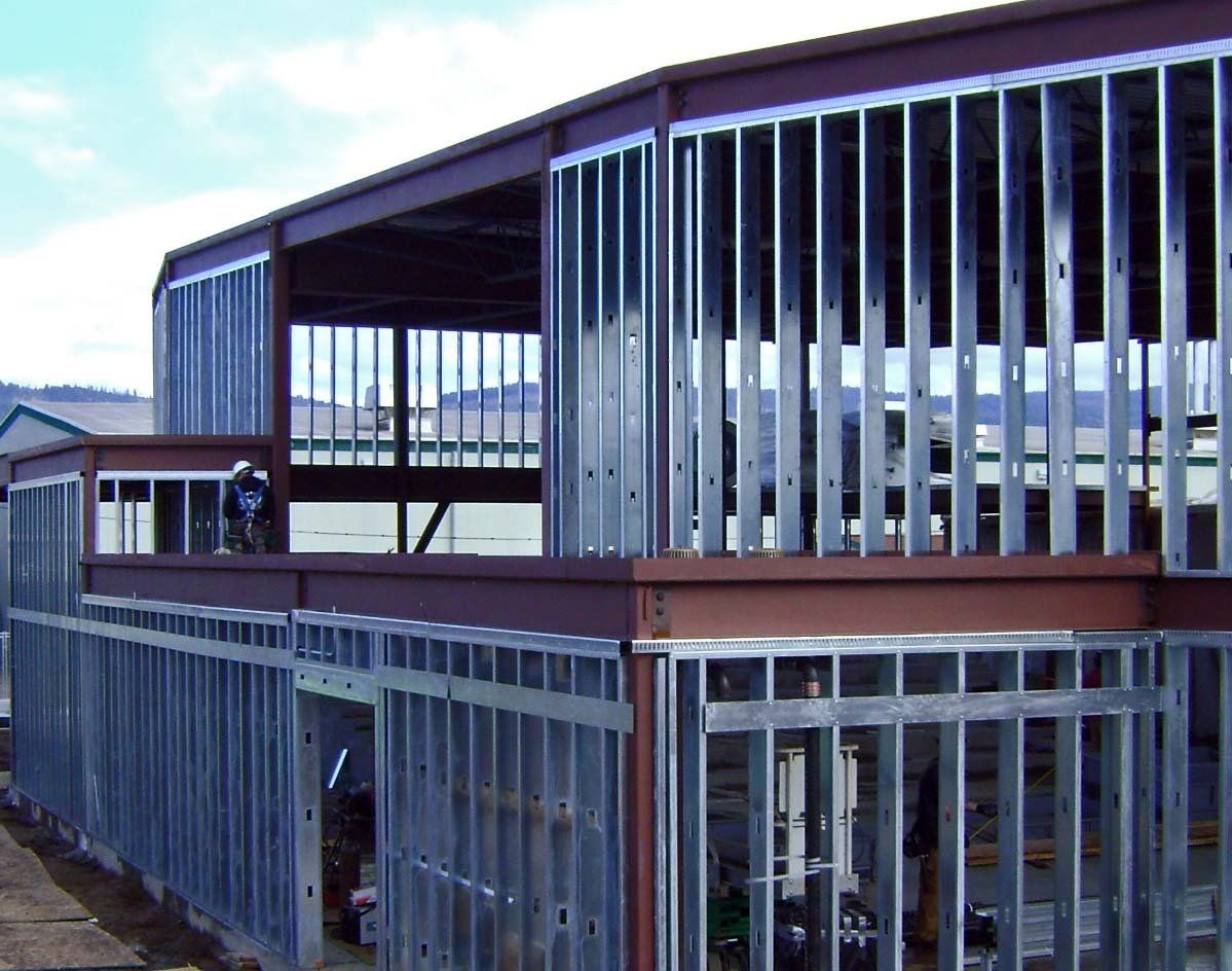 Steel framing for a building under construction, exterior view. Gray metal beams and studs. Brown horizontal beams.