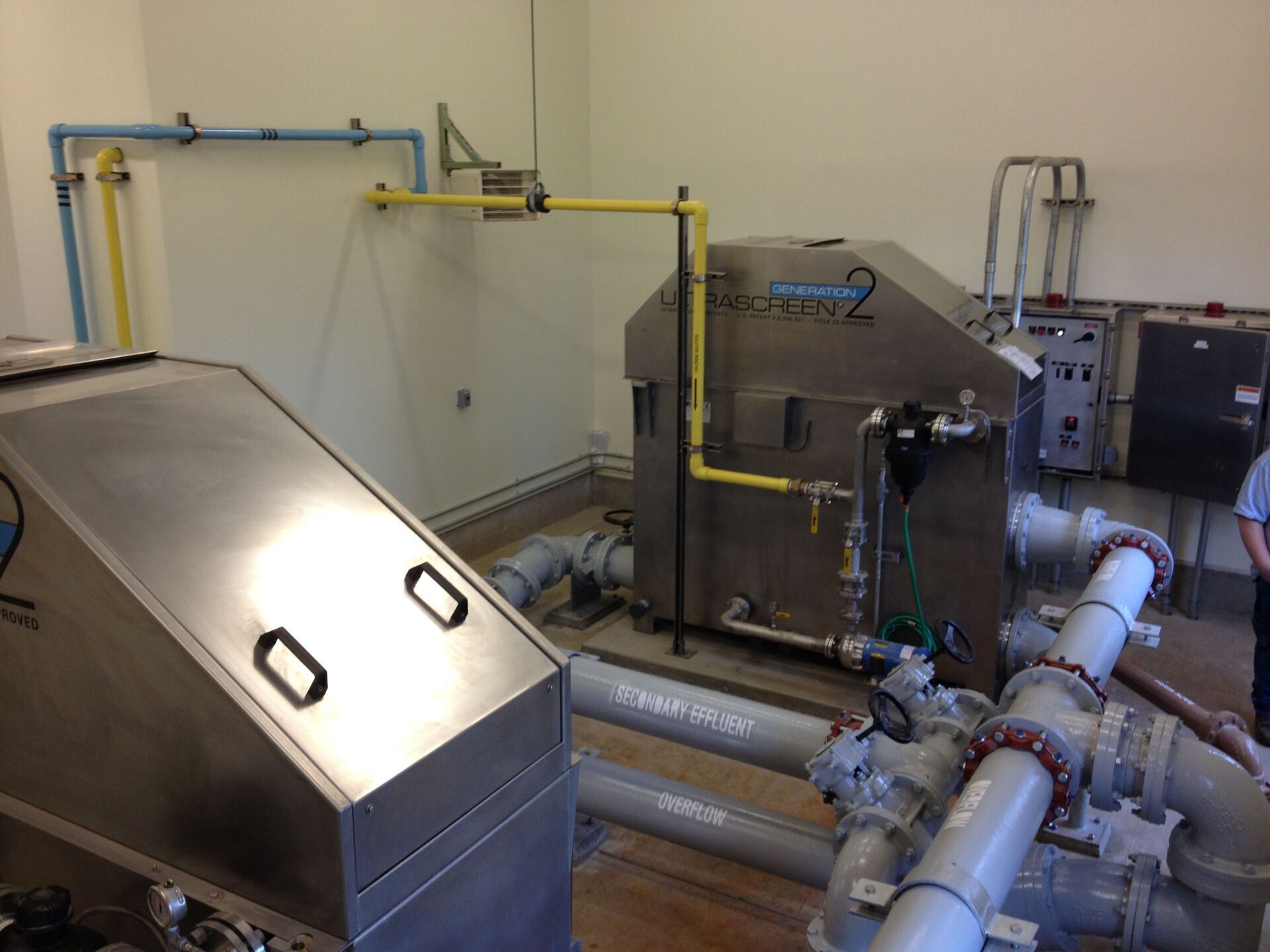 Water filtration system with metal tanks, pipes, and gauges in a utility room.