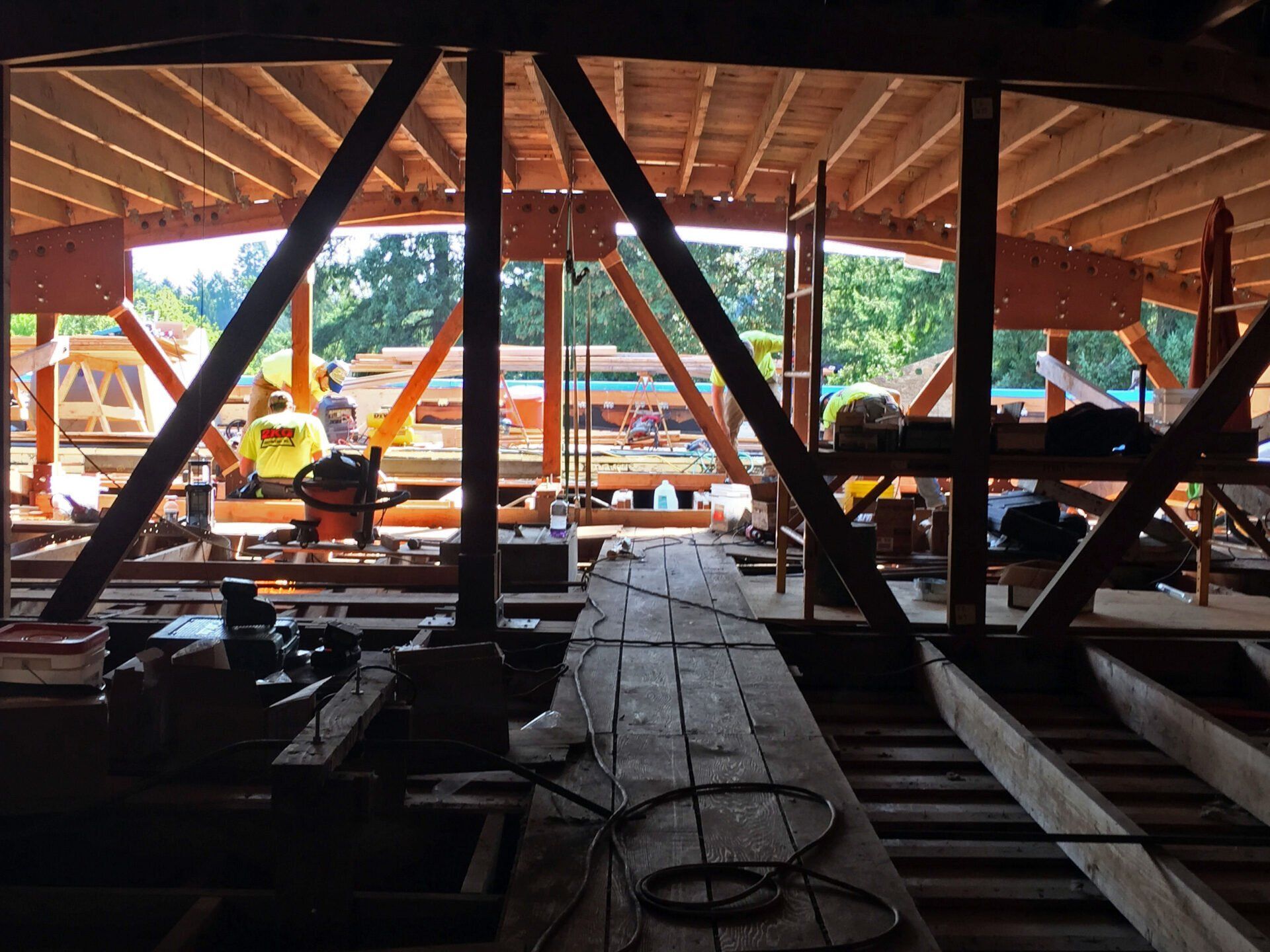 Construction site: Wooden beams supporting a roof. Workers in yellow vests.
