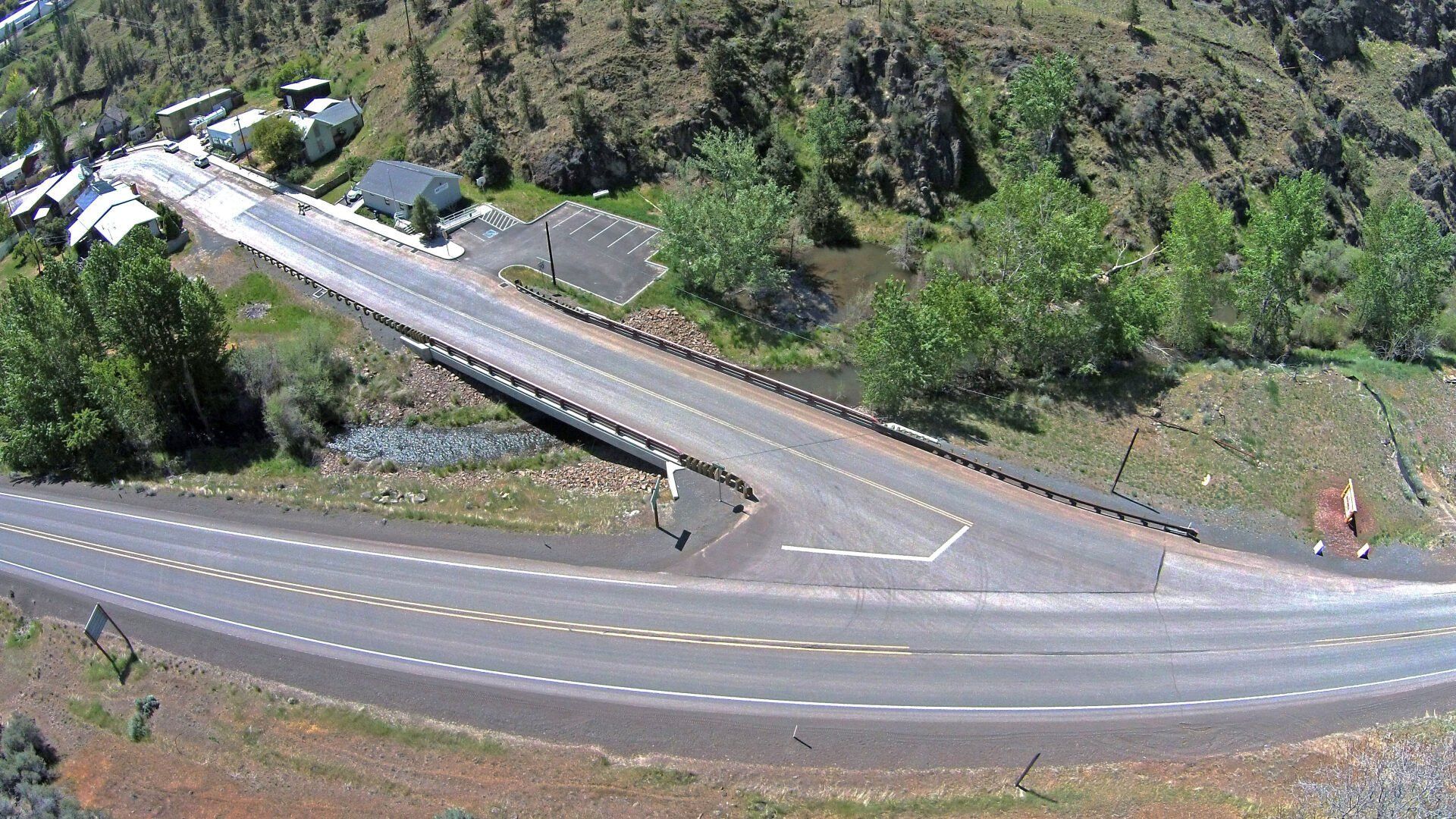 Overhead view of a bridge crossing a road, surrounded by trees and mountains.