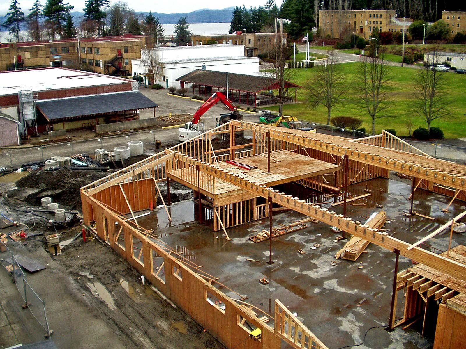 Construction site: wood frame building under construction, exterior view with town and water in background.