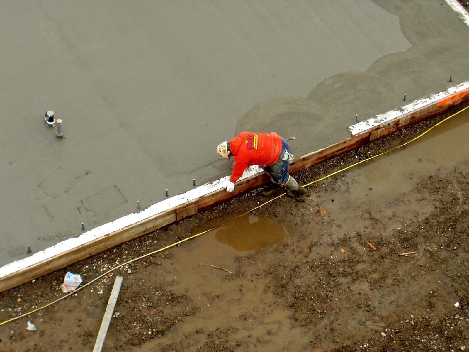 Construction worker in red jacket working on wet concrete.