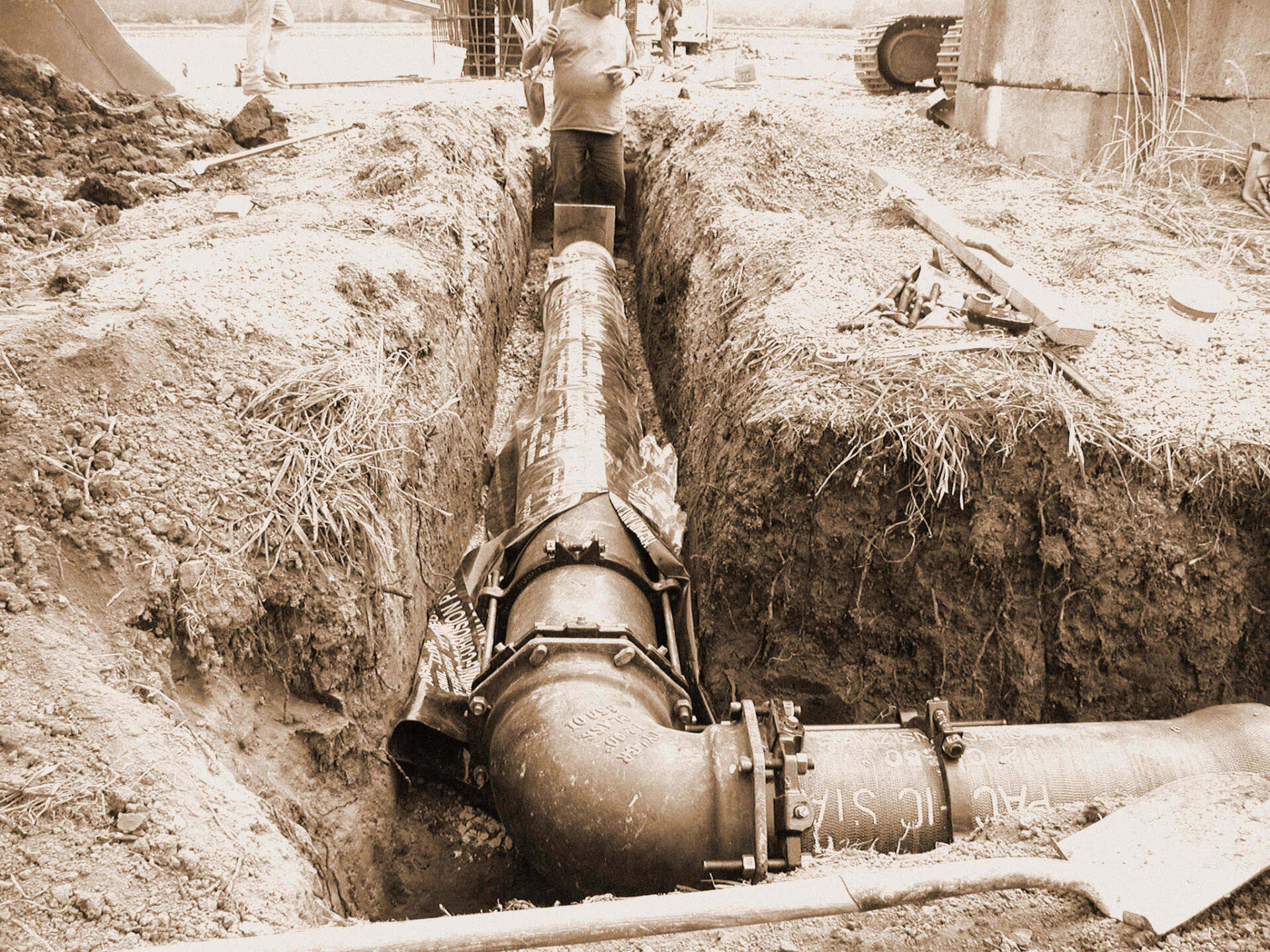 A large metal pipe being installed in a trench. Workers are in the background.