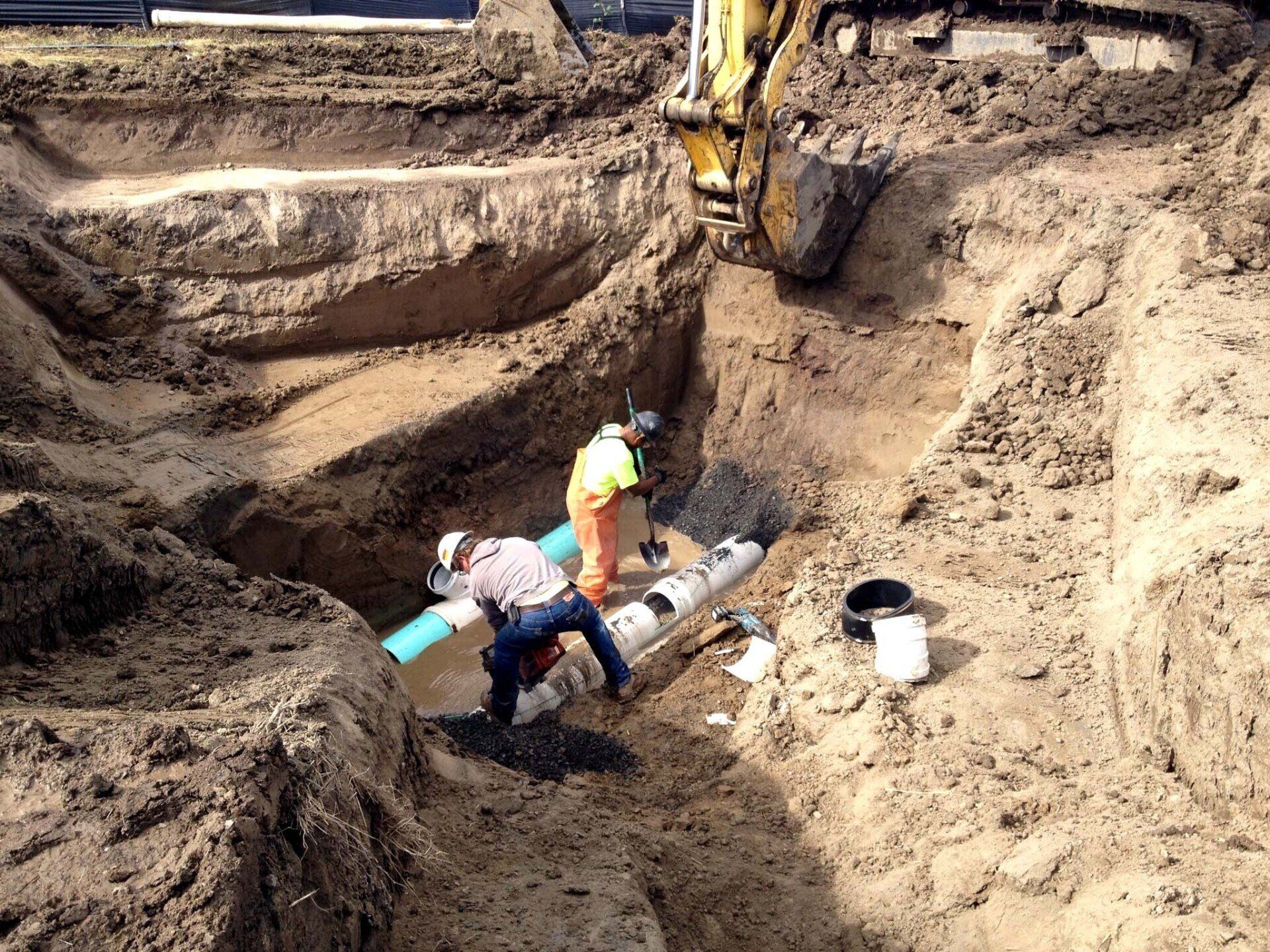 Workers installing pipe in a deep trench at a construction site.