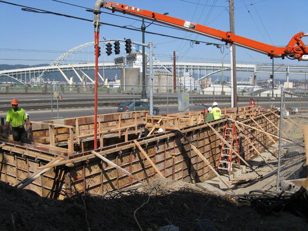 Construction workers pouring concrete into wooden forms at a construction site with an orange boom lift.