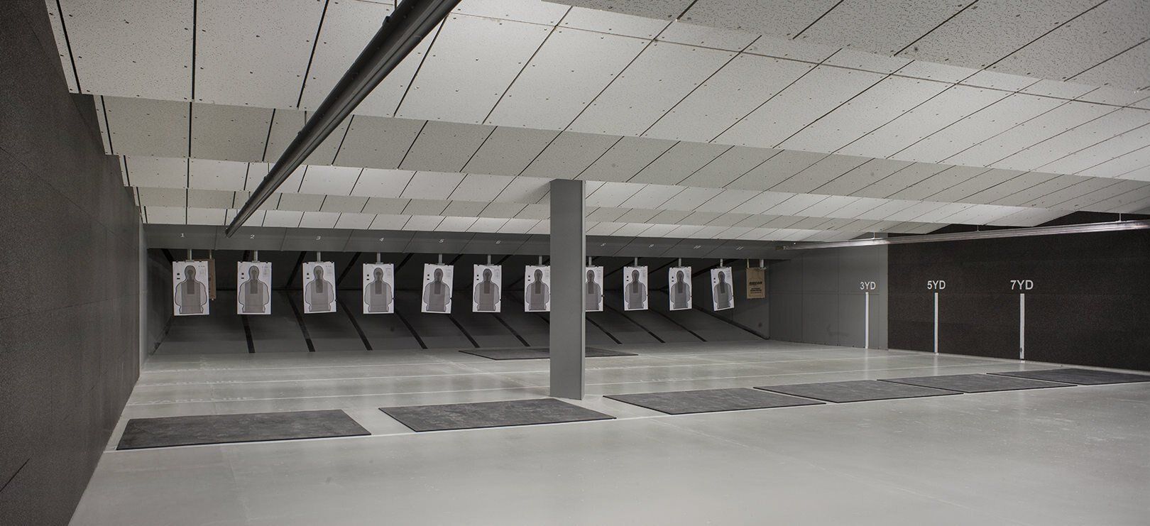 An indoor shooting range with paper targets hanging. Gray walls, ceiling, and floor.