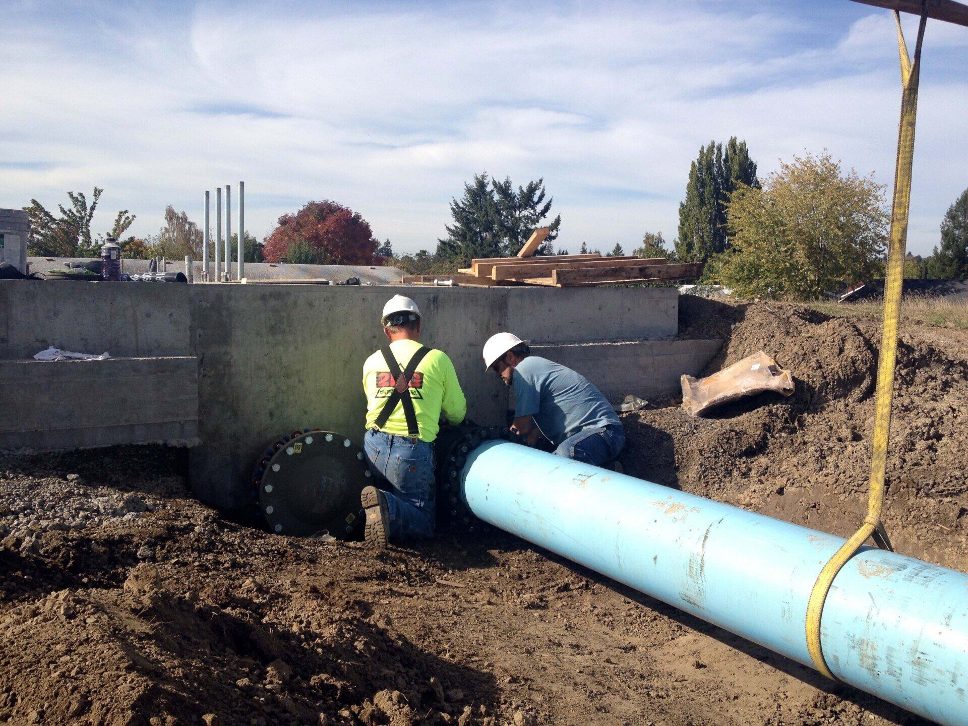 Two workers connecting a blue water pipe to a concrete structure in an outdoor construction site.