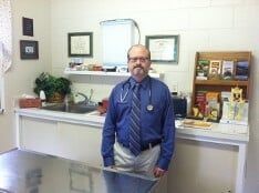 A man in a blue shirt and tie is standing in a veterinary office.