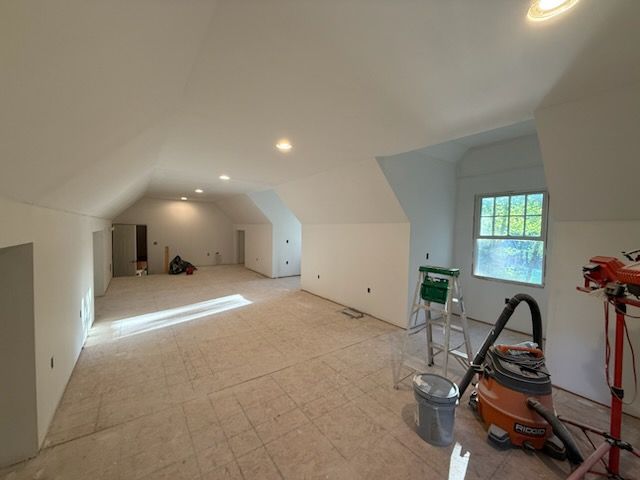 Interior view of an unfinished room with white walls, recessed lighting, and a window.