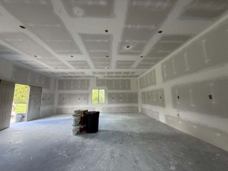 Interior of a room under construction with drywall on walls and ceiling, a window, and a concrete floor.