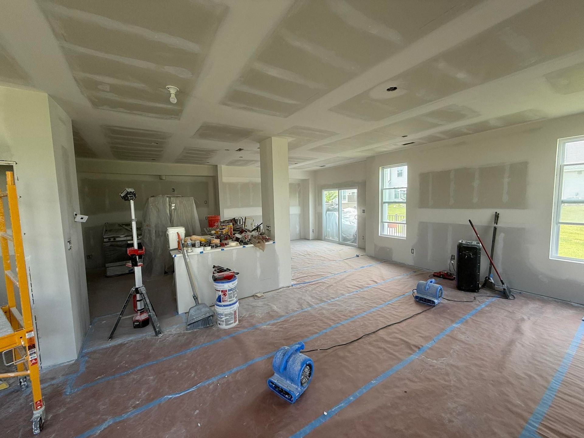 Interior view of a room under construction with drywall installed on walls and ceiling. Protective paper covers the floor.