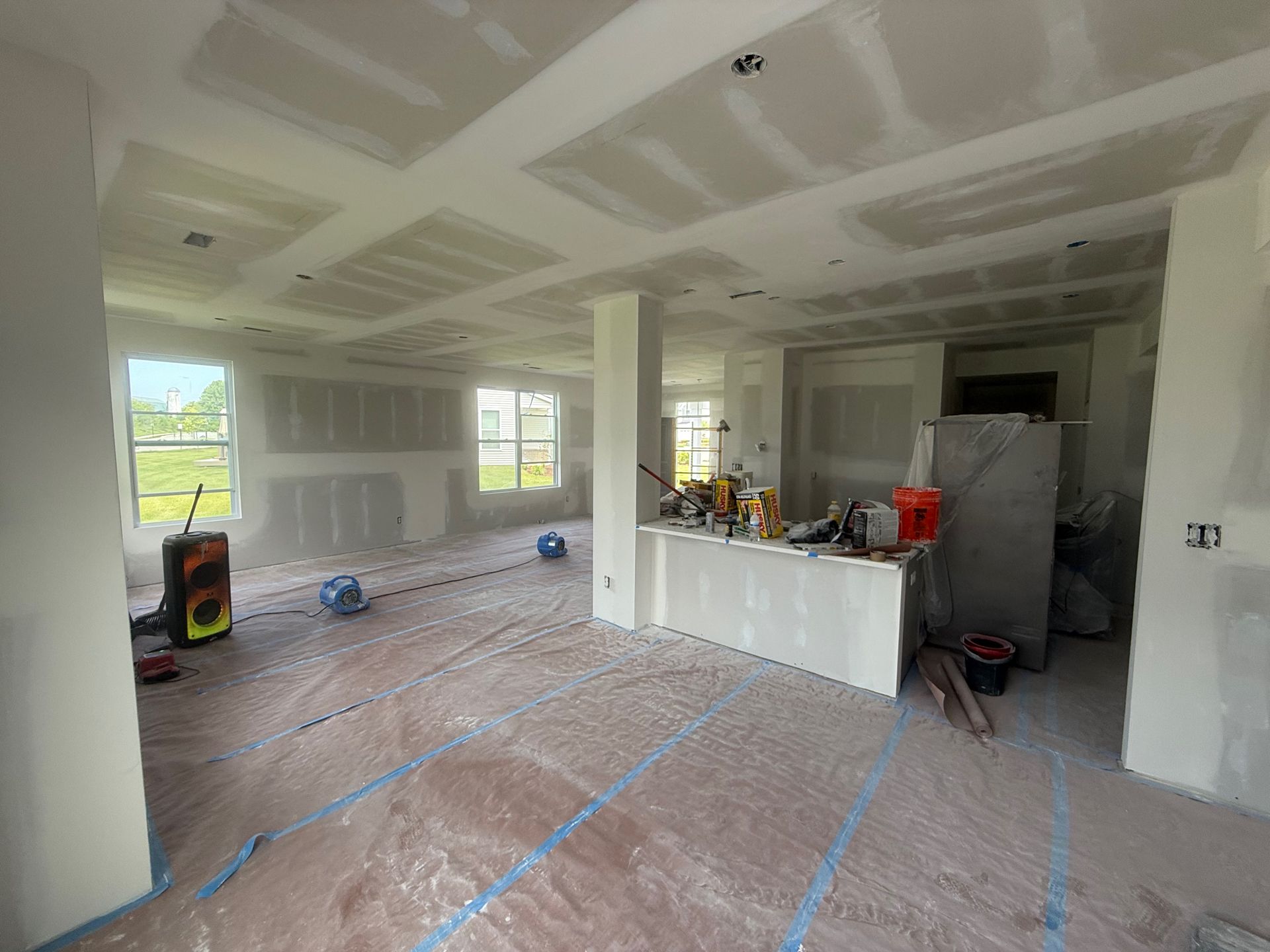 Interior of a room under construction, with drywall on walls and ceiling. Tools and materials are present.