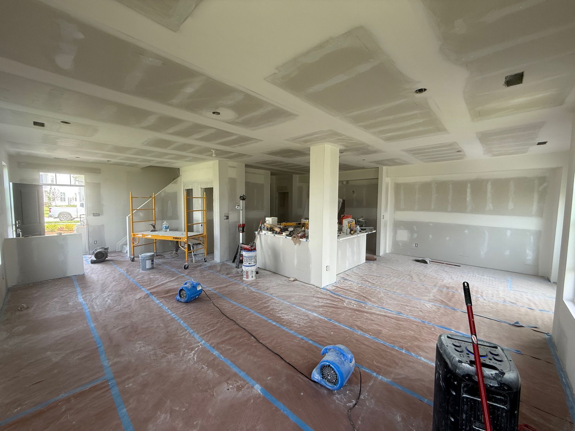 Interior under construction; drywall installation with drying fans and exposed wiring.
