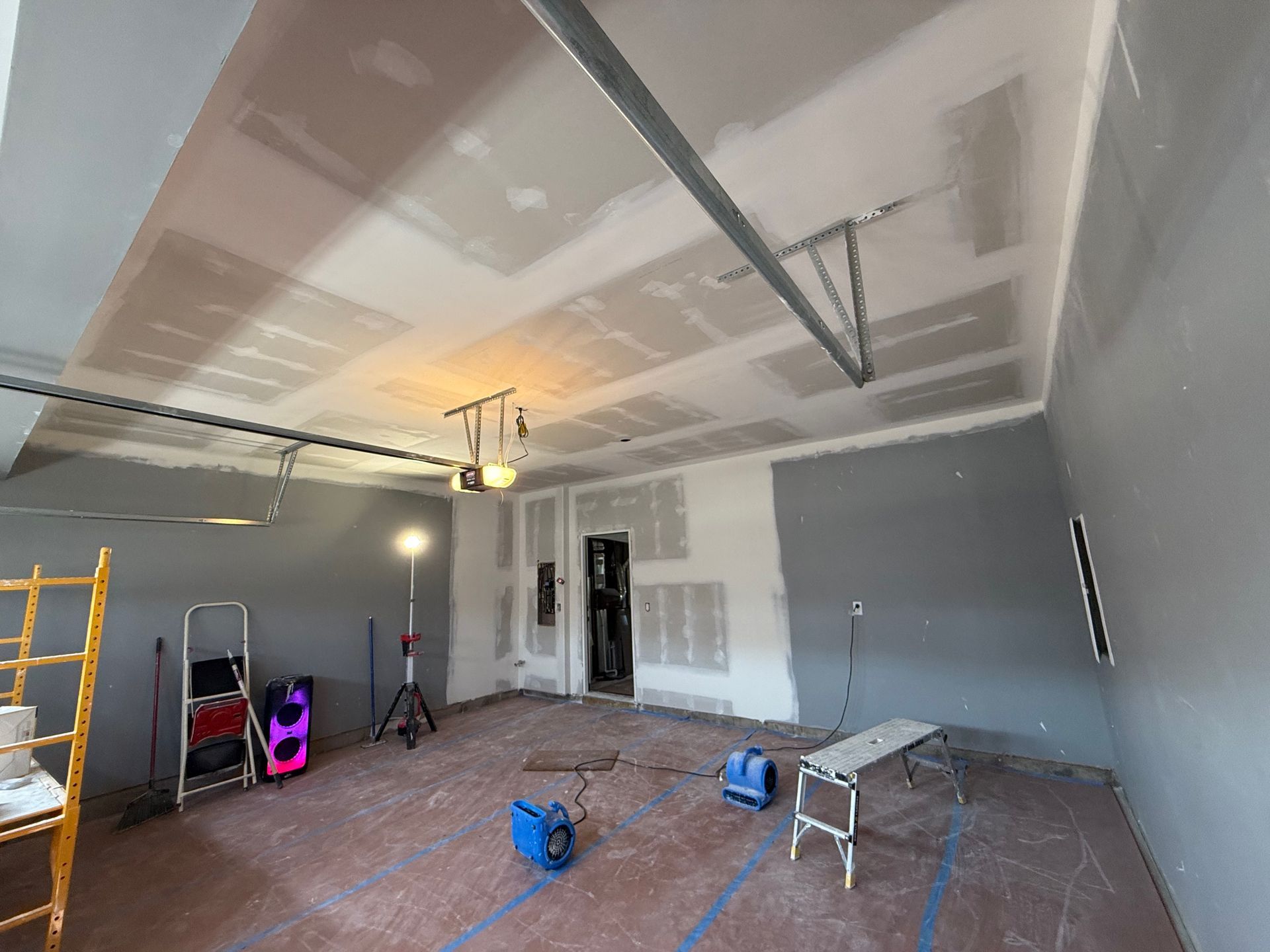 Garage interior under renovation; drywall, ladder, tools, and a bench.