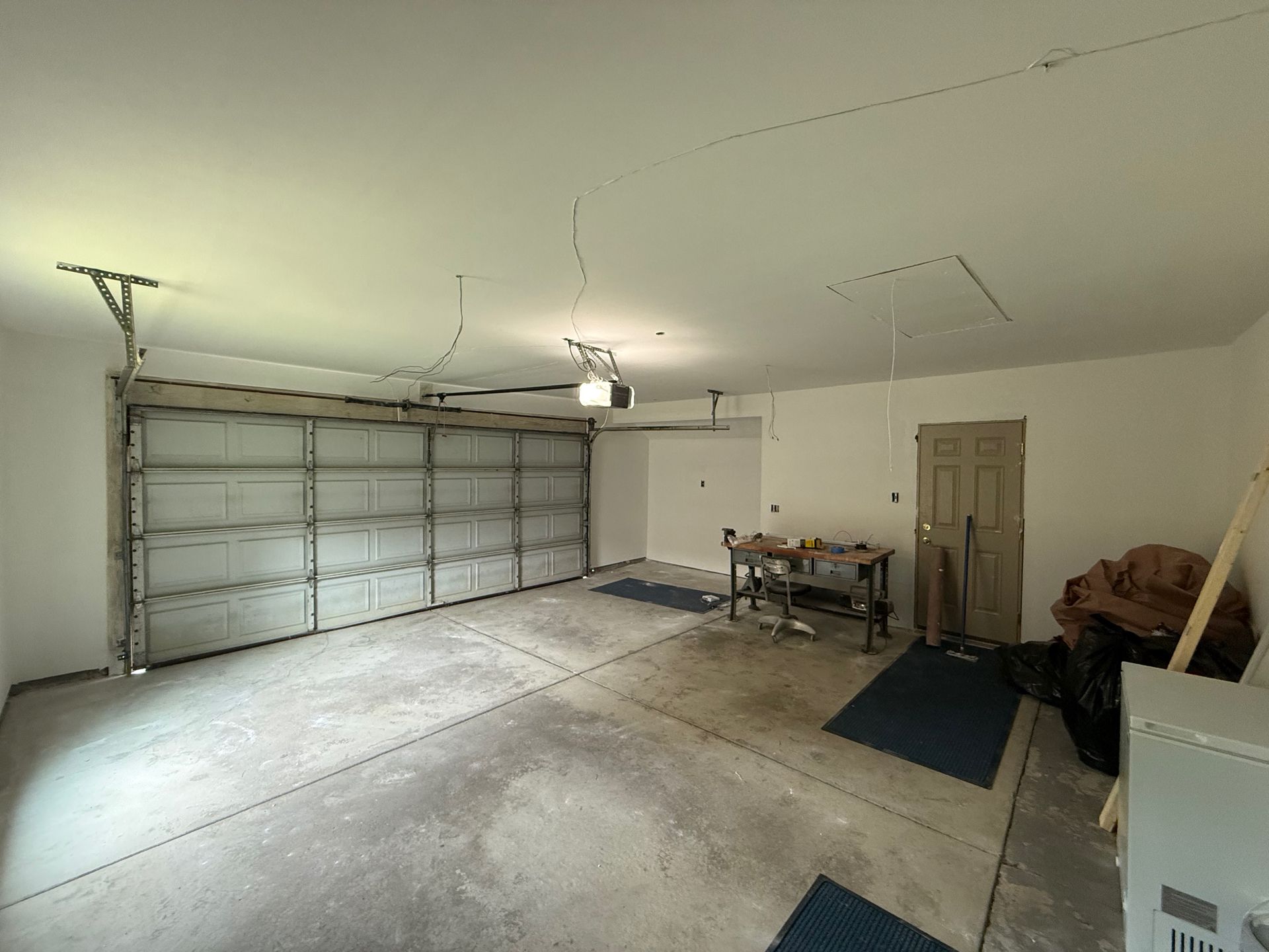 Garage interior with open door, work table, and storage. Gray concrete floor, white walls and ceiling.