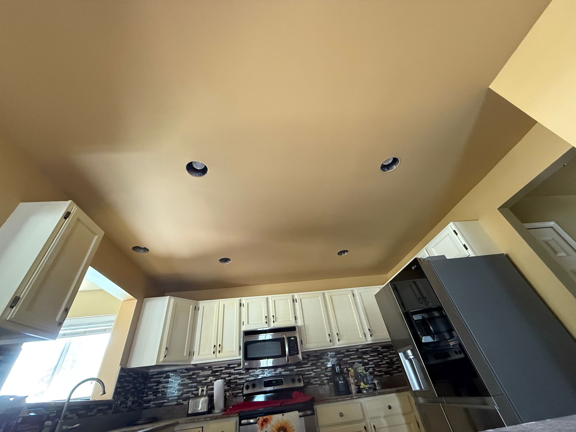 Kitchen ceiling with recessed lighting above white cabinets, appliances, and backsplash.