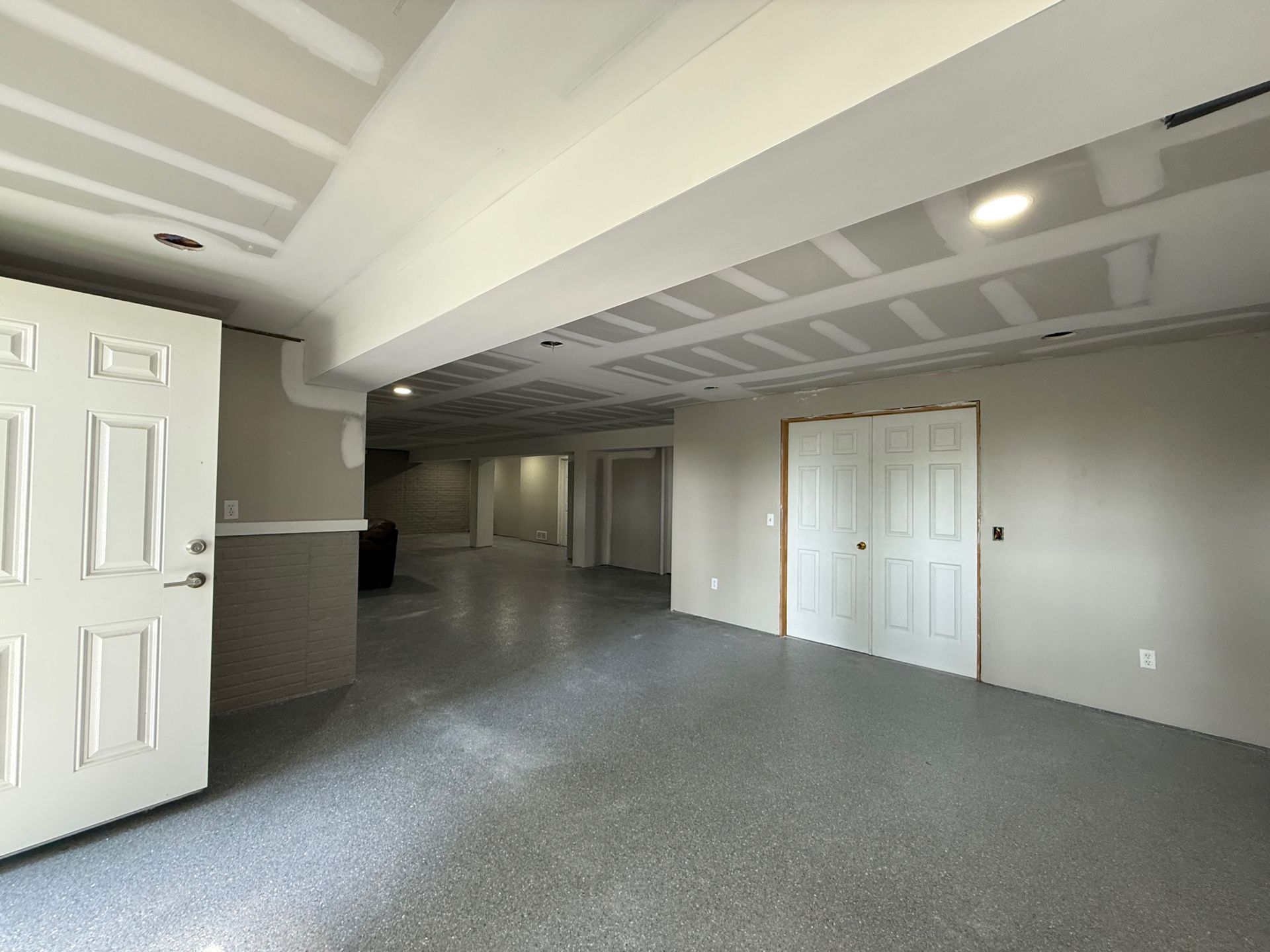Empty basement with gray epoxy floor, white doors, and unfinished ceiling.